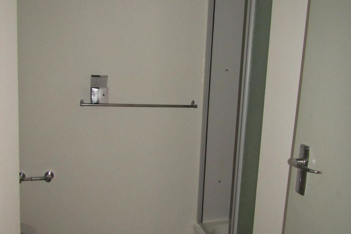 A functional bathroom featuring a shower enclosure and tiled flooring, presented in a clean, neutral, and empty state.