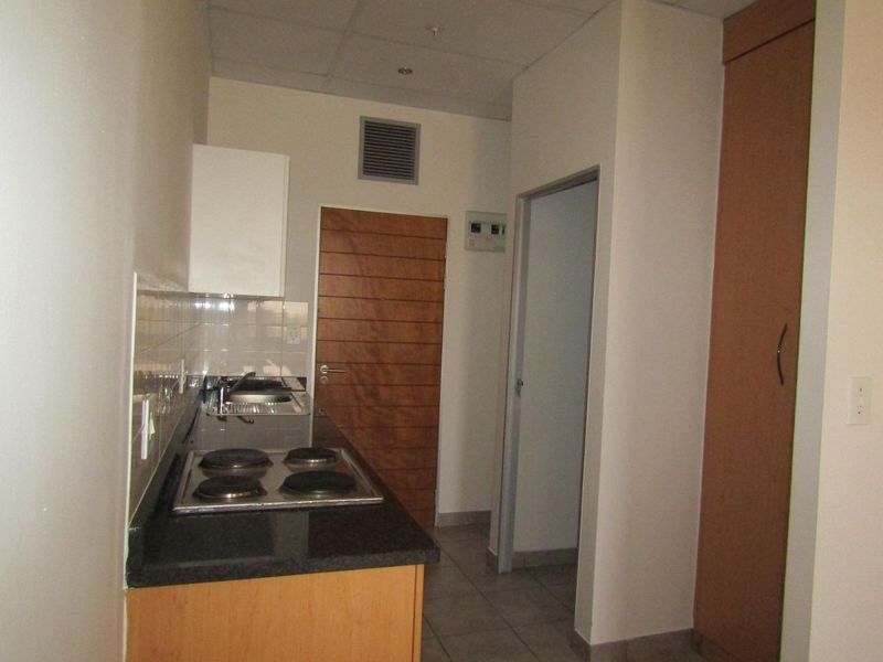 Compact kitchen featuring built-in cabinetry, an electric hob, stainless steel sink, and tiled flooring, offering a functional and efficient workspace.