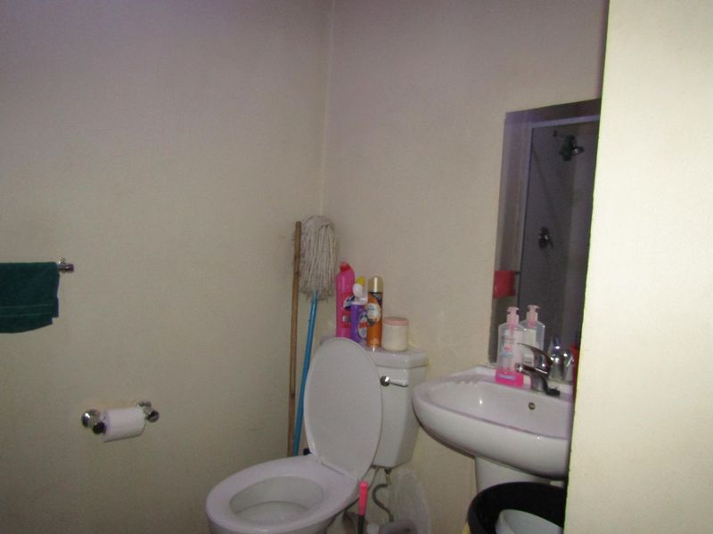 A functional bathroom featuring a pedestal washbasin, toilet, and wall-mounted mirror, providing essential sanitary facilities.