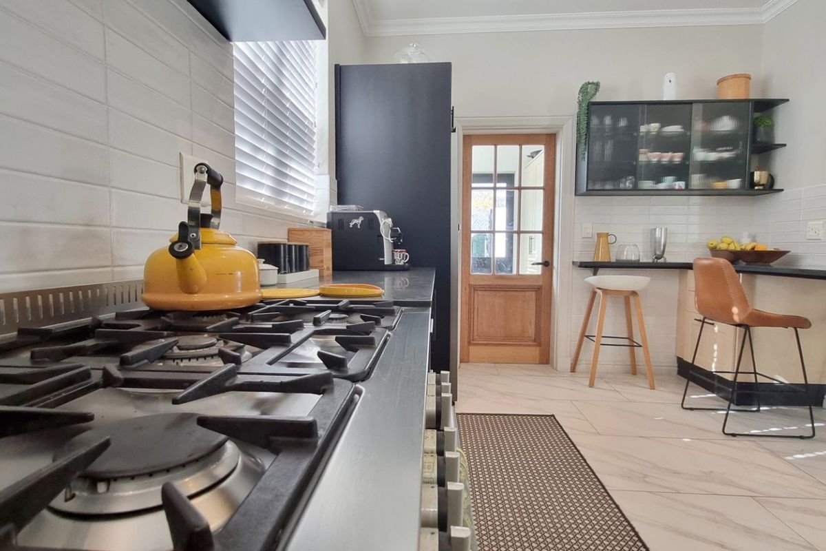 Modern kitchen featuring a stainless steel gas cooktop, tiled backsplash, breakfast bar, and dark cabinetry with a classic timber door.