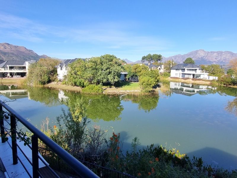 Scenic elevated view overlooking a tranquil lake and surrounding residential estate with mountain vistas in the background.