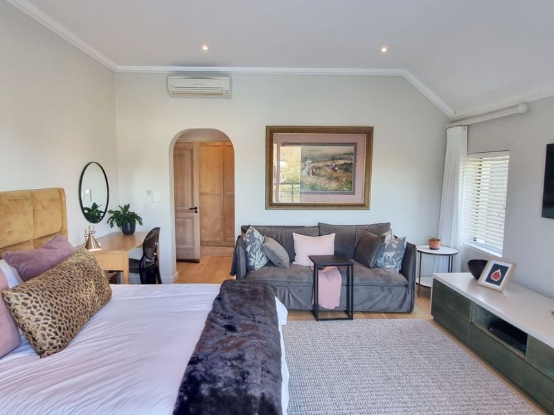 Spacious bedroom featuring timber flooring, recessed downlighting, a split-system air conditioner, and an arched doorway leading to an adjoining space.