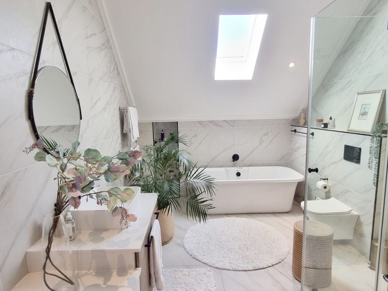Modern bathroom featuring a freestanding bathtub, glass-enclosed shower, wall-mounted toilet, and a skylight, finished with elegant marble-look tiling.