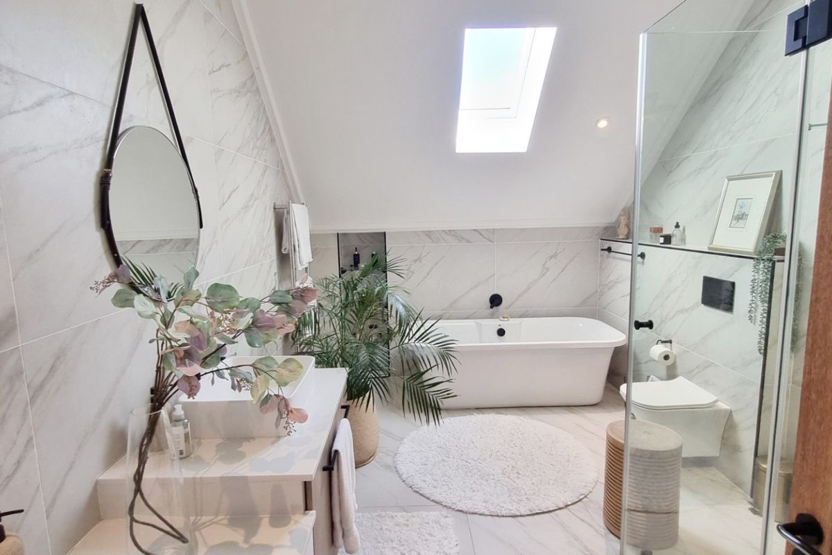 Modern bathroom featuring a freestanding bathtub, glass-enclosed shower, wall-mounted toilet, and a skylight, finished with elegant marble-look tiling.