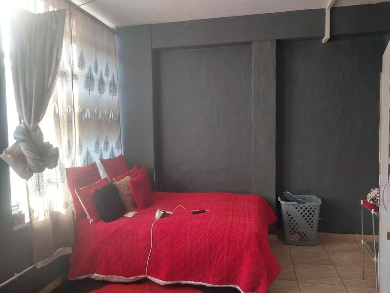 A bedroom featuring dark painted walls and tiled flooring, illuminated by natural light from a large window.