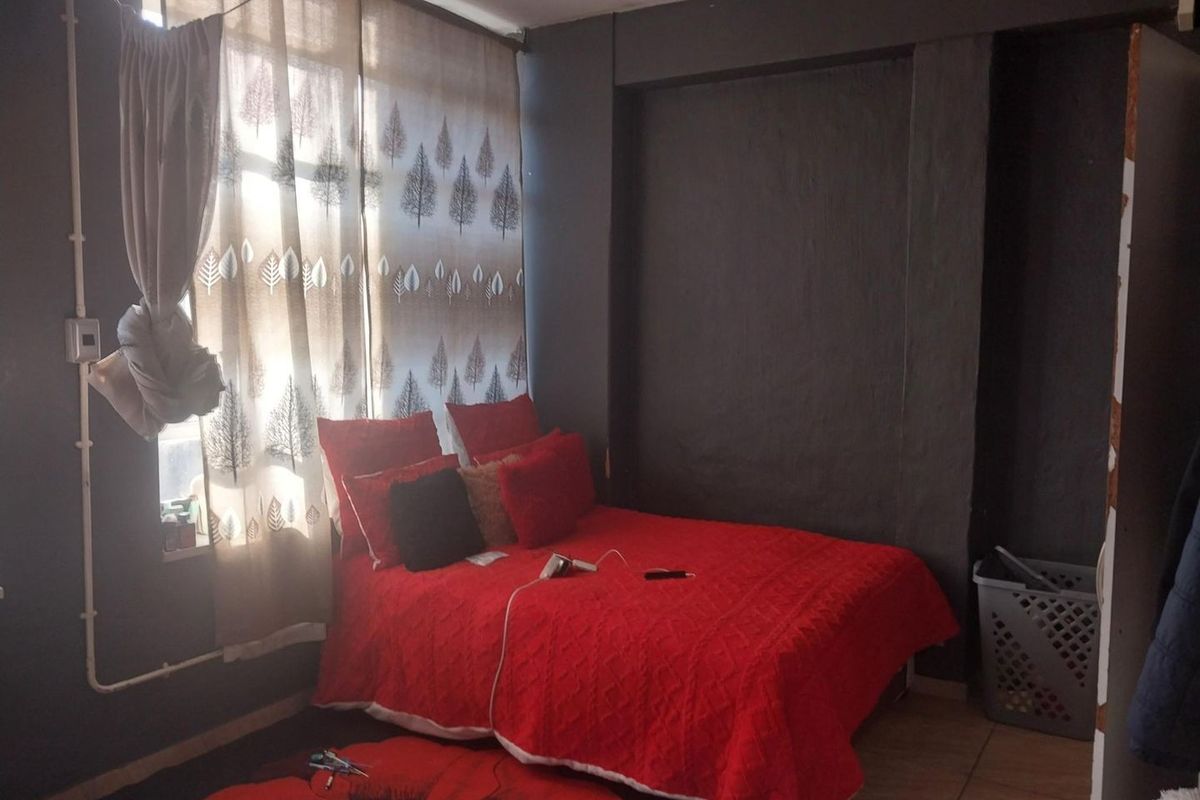 A bedroom featuring tiled flooring and dark painted walls with exposed electrical conduit, requiring cosmetic updates to improve the overall aesthetic.