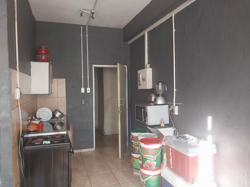 A compact kitchen area featuring tiled flooring, a built-in stove, and exposed electrical conduit, requiring cosmetic updates to improve its overall aesthetic and functionality.