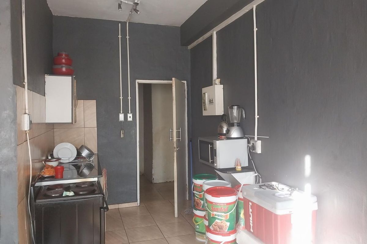 A compact kitchen area featuring tiled flooring, a built-in stove, and exposed electrical conduit, requiring cosmetic updates to improve its overall aesthetic and functionality.