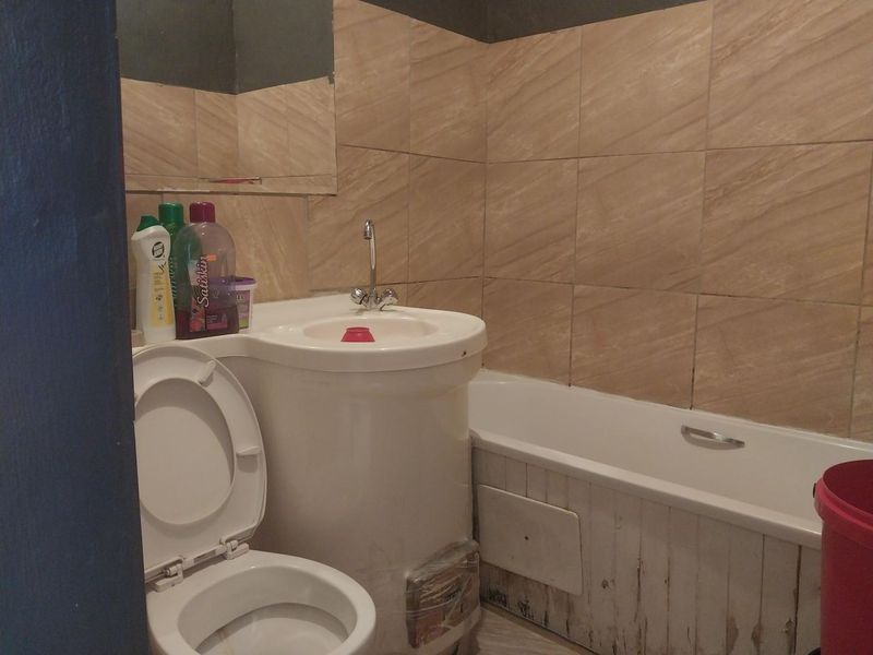 A compact bathroom featuring a pedestal sink, bathtub, and toilet with tiled wall finishes, currently showing signs of wear and maintenance needs.