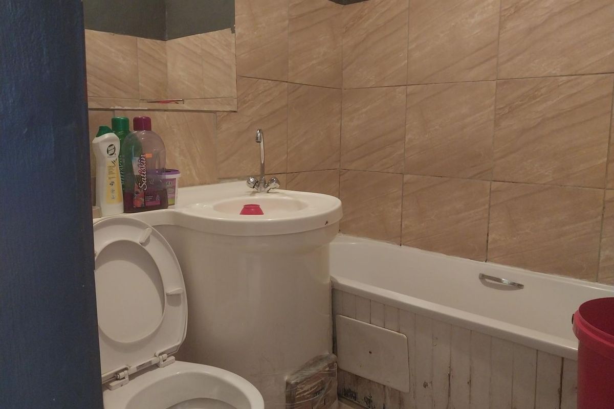 A compact bathroom featuring a pedestal sink, bathtub, and toilet with tiled wall finishes, currently showing signs of wear and maintenance needs.