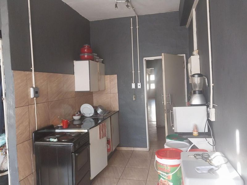 A compact kitchen featuring tiled flooring, a tiled backsplash, and built-in cabinetry, with visible surface-mounted electrical conduit throughout the space.