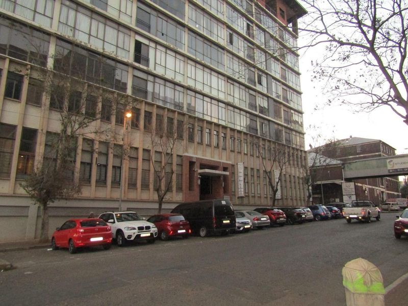 Street-level view of a multi-story apartment building featuring a large glass facade and concrete structural elements.
