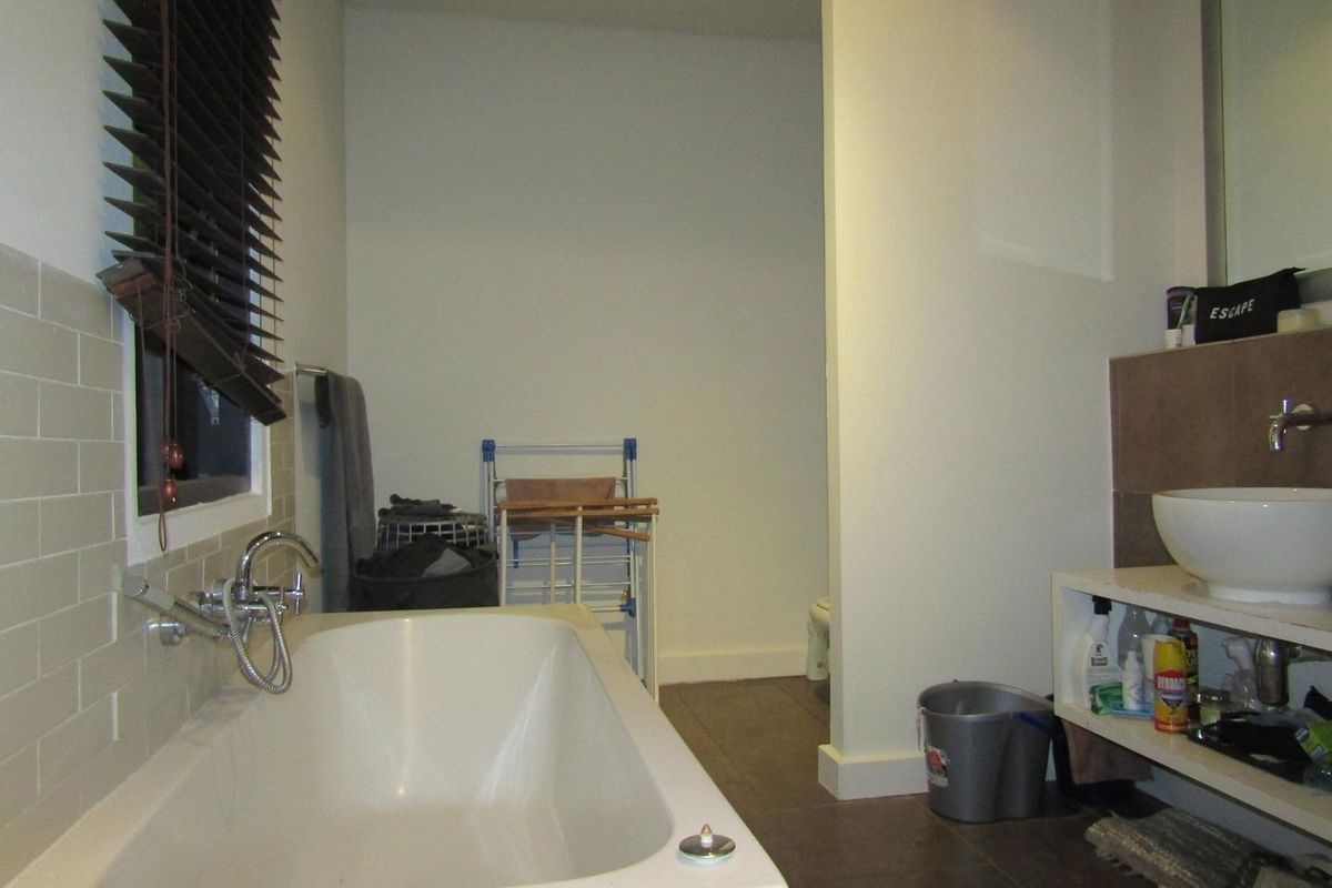 A functional bathroom featuring a built-in bathtub with wall-mounted fixtures, a vessel sink vanity, and neutral wall tiling.