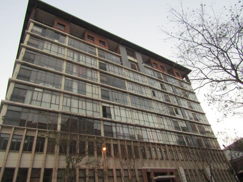 A multi-story apartment building facade featuring extensive glass windows and balconies, showing signs of age and exterior wear.