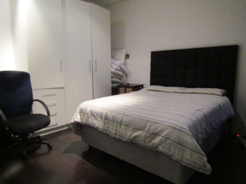 A functional bedroom featuring built-in white cabinetry and dark laminate flooring, providing essential storage and a neutral foundation for personal styling.