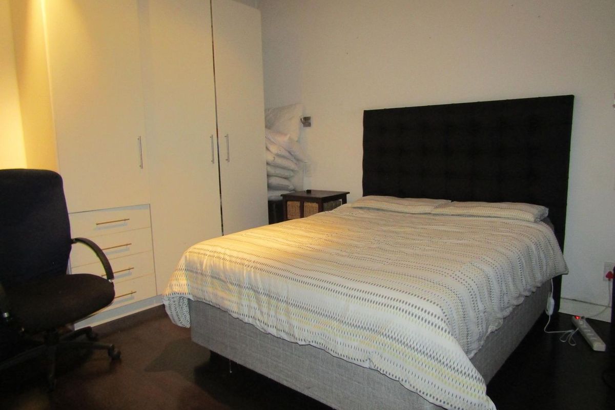 A bedroom featuring dark laminate flooring and a white built-in wardrobe with integrated drawers.