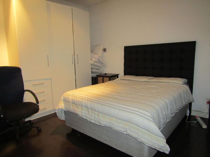 A bedroom featuring dark laminate flooring and a white built-in wardrobe with integrated drawers.