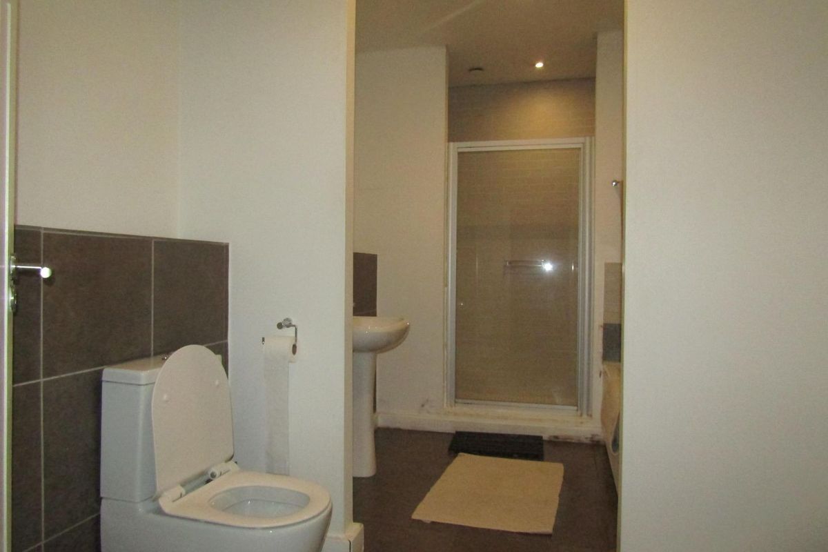 A functional bathroom featuring a pedestal basin, a separate shower enclosure, and a toilet with neutral wall and floor tiling.