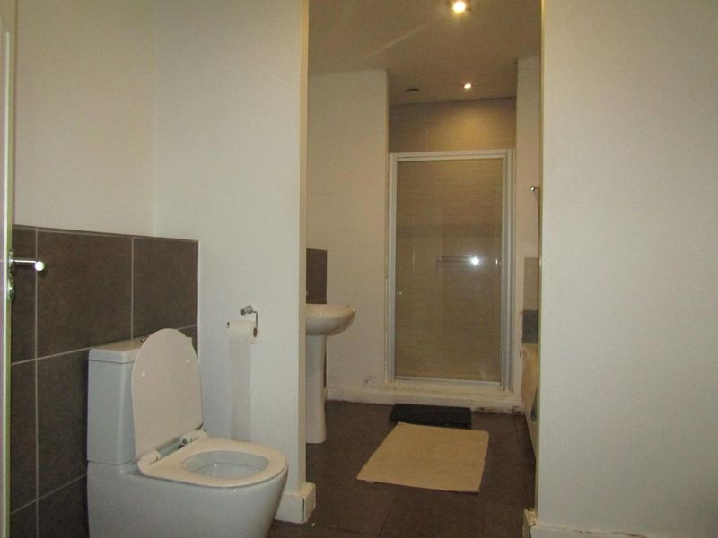 A functional bathroom featuring a pedestal basin, a separate shower enclosure, and a toilet with neutral wall and floor tiling.