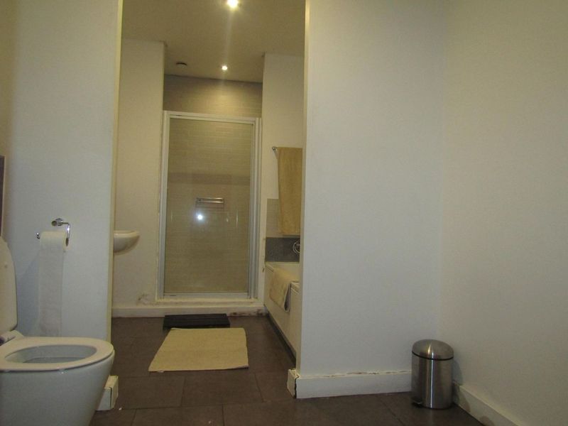 A functional bathroom featuring a shower enclosure, bathtub, and wall-mounted basin with tiled flooring and recessed lighting.