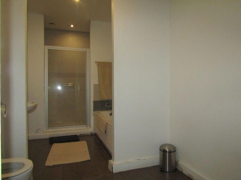 A functional bathroom featuring a shower enclosure, bathtub, toilet, and wall-mounted basin with tiled flooring and recessed lighting.