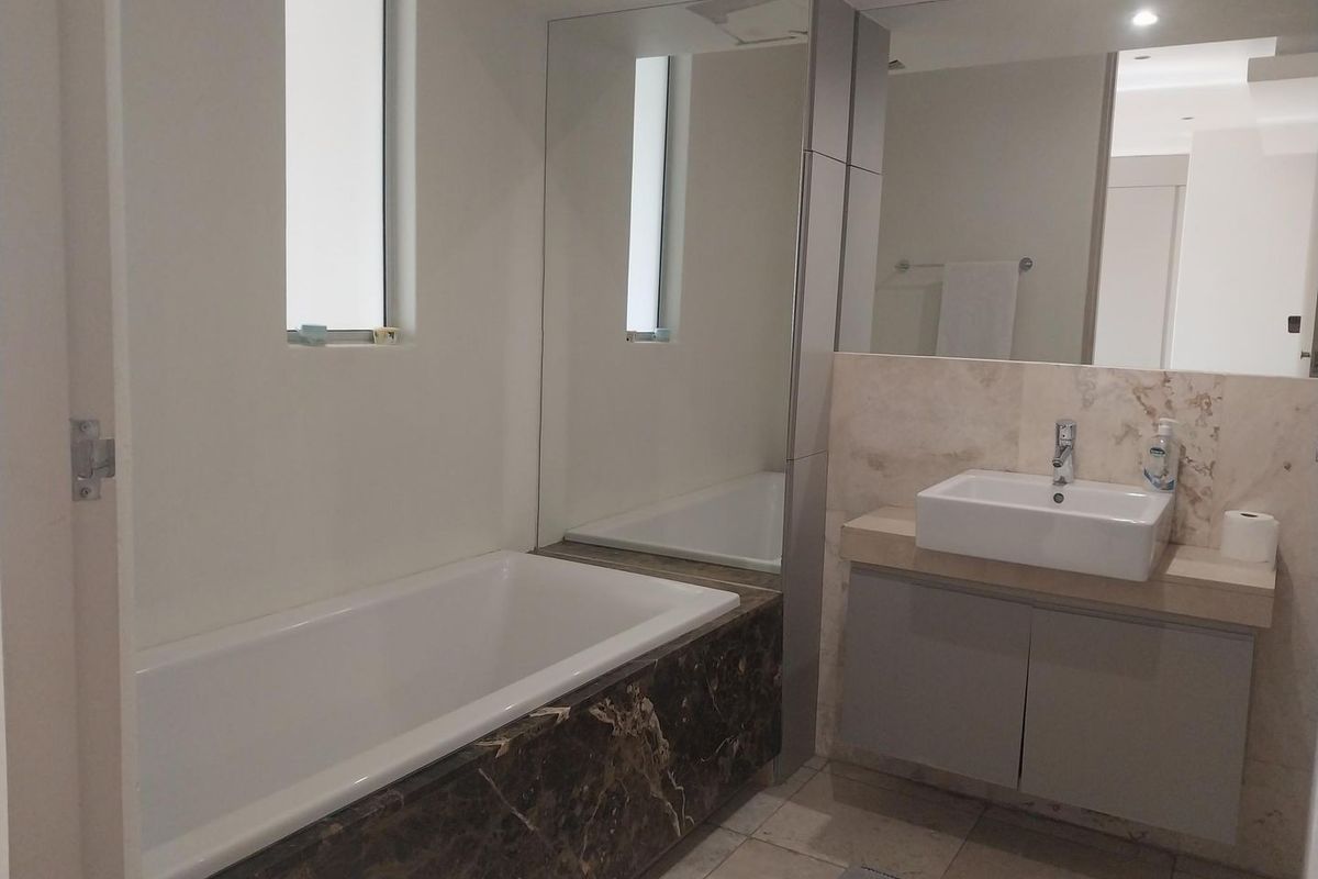 Modern bathroom featuring a built-in bathtub with marble surround, a stone-topped vanity with vessel sink, and large wall-mounted mirrors.