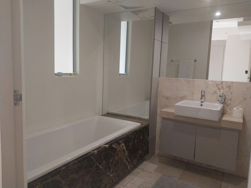 Modern bathroom featuring a built-in bathtub with marble surround, a stone-topped vanity with vessel sink, and large wall-mounted mirrors.
