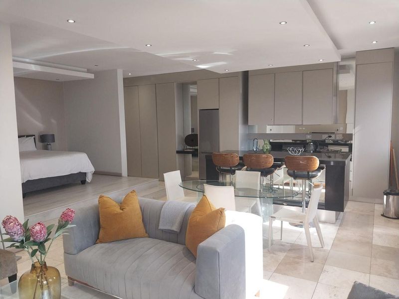 Modern open-plan apartment featuring a sleek kitchen with integrated cabinetry and island, flowing into a combined living and bedroom area with recessed lighting.