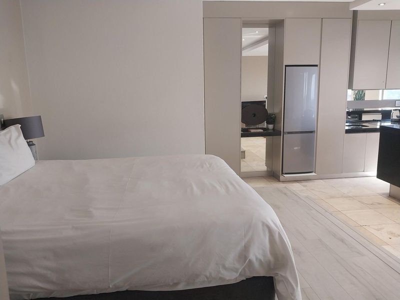 An open-plan apartment layout featuring a bedroom area adjacent to a modern kitchen with sleek built-in cabinetry and neutral flooring.