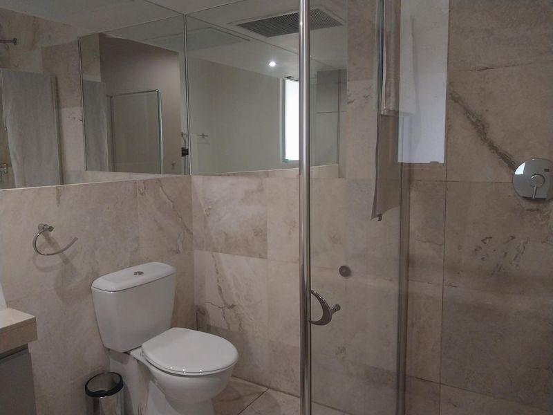 A modern bathroom featuring stone wall and floor tiles, a glass shower enclosure, and a large wall-mounted mirror.