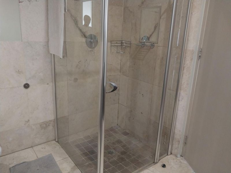 A functional bathroom featuring a glass-enclosed shower with stone tiling and integrated fixtures.