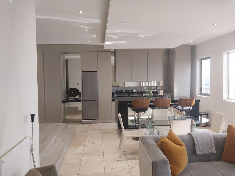 Modern open-plan living area featuring a sleek kitchen with integrated cabinetry, stone tile flooring, and a raised platform, creating a seamless flow.