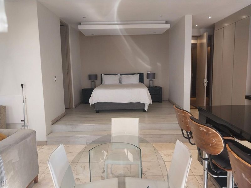 A modern bedroom area featuring a raised platform design, recessed ceiling lighting, and integrated storage cupboards, creating a distinct sleeping zone within the apartment.