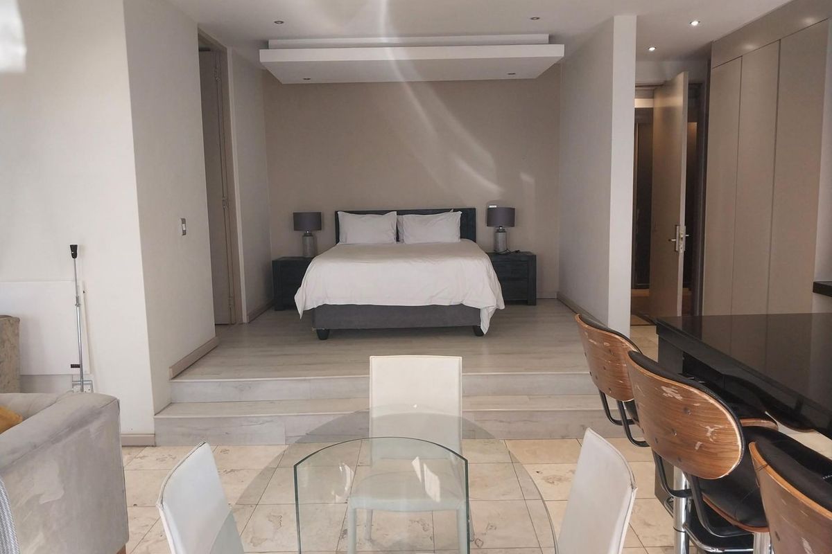 A modern bedroom area featuring a raised platform design, recessed ceiling lighting, and integrated storage cupboards, creating a distinct sleeping zone within the apartment.