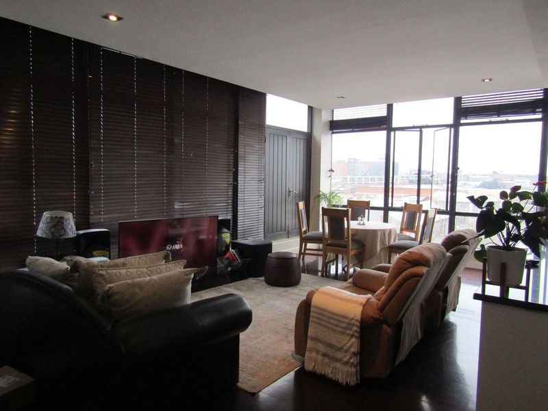 Spacious open-plan living and dining area featuring dark wood flooring, recessed lighting, and expansive windows providing ample natural light and urban views.