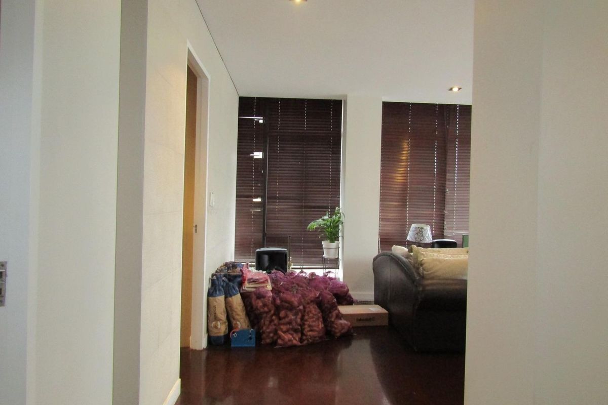 A living room area featuring dark timber flooring, recessed downlighting, and large windows fitted with dark venetian blinds.