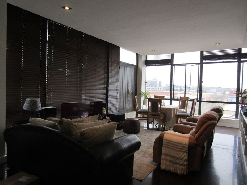 Spacious open-plan living and dining area featuring dark wood flooring, recessed lighting, and expansive windows with city views.