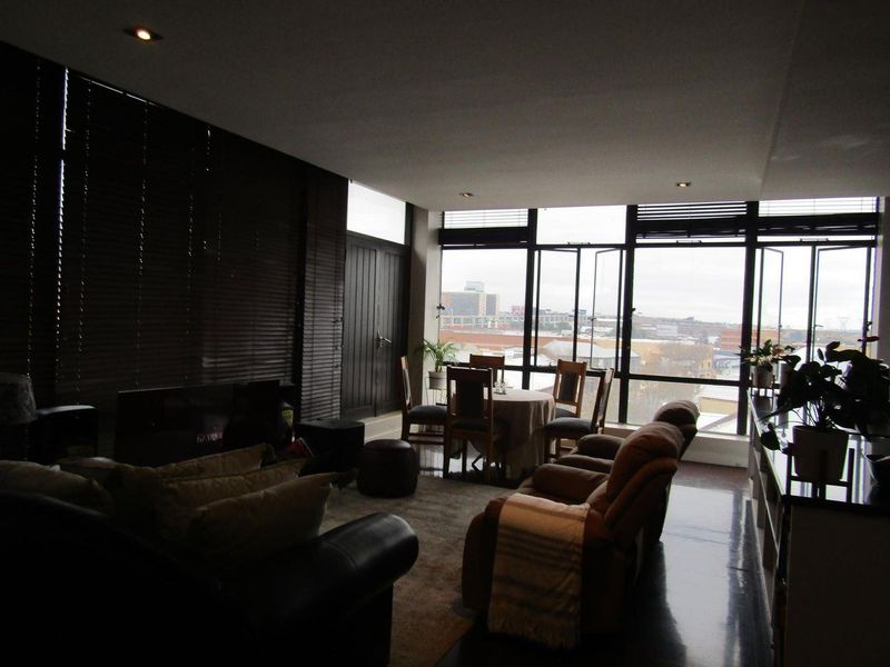 Spacious open-plan living and dining area featuring large windows with city views, dark flooring, and recessed lighting.