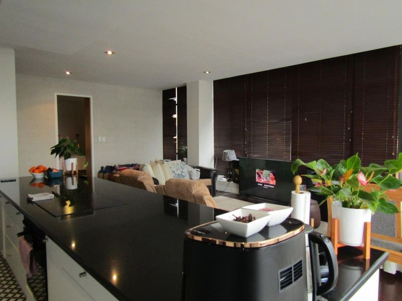 Open-plan living area featuring a modern kitchen with a large black granite island, recessed lighting, and dark venetian blinds.