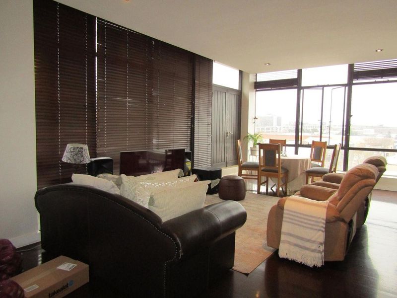 Spacious open-plan living and dining area featuring dark wood flooring, large windows with venetian blinds, and recessed lighting.