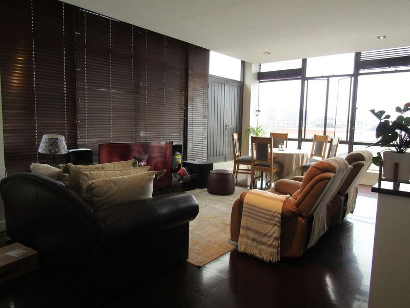 Spacious open-plan living and dining area featuring dark wood flooring, large windows with venetian blinds, and recessed lighting.