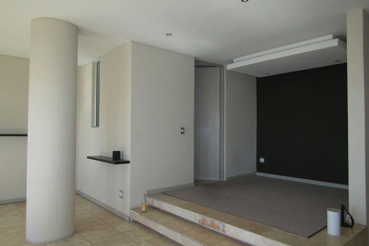 An open-plan living area featuring a raised platform, a structural column, and a dark feature wall, offering a versatile space for interior design.