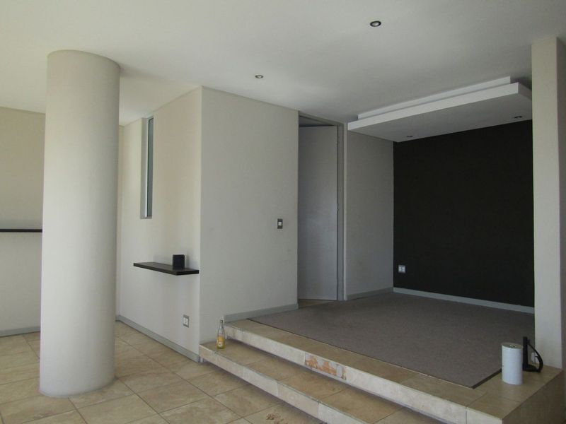 An open-plan living area featuring a raised platform, a structural column, and a dark feature wall, offering a versatile space for interior design.