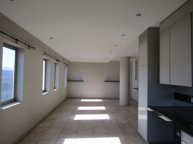 An open-plan living and kitchen area featuring tiled floors, recessed lighting, a structural column, and modern built-in cabinetry with stone countertops.