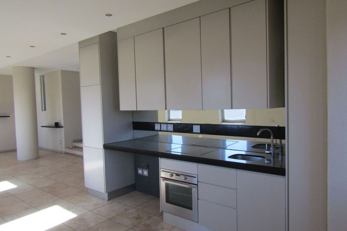Modern kitchen featuring sleek cabinetry, dark stone countertops, integrated oven, and cooktop, set within an open-plan living space with tiled flooring.