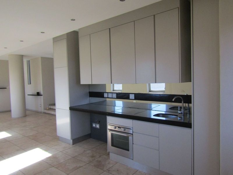 Modern kitchen featuring sleek cabinetry, dark stone countertops, integrated oven, and cooktop, set within an open-plan living space with tiled flooring.