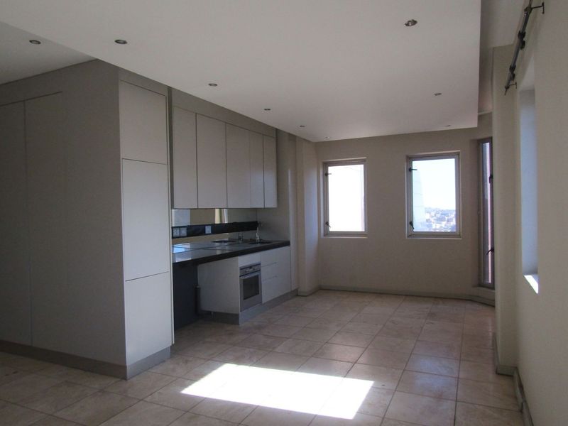 An open-plan living and kitchen area featuring neutral cabinetry, integrated oven, tiled flooring, and large windows providing natural light.