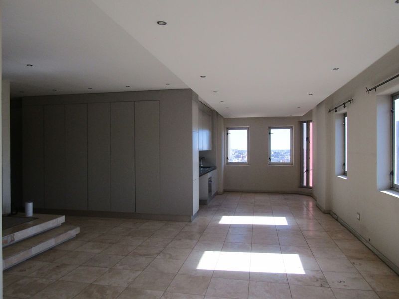 Spacious open-plan living area featuring tiled flooring, recessed lighting, and a compact integrated kitchen with built-in cabinetry and stone countertops.