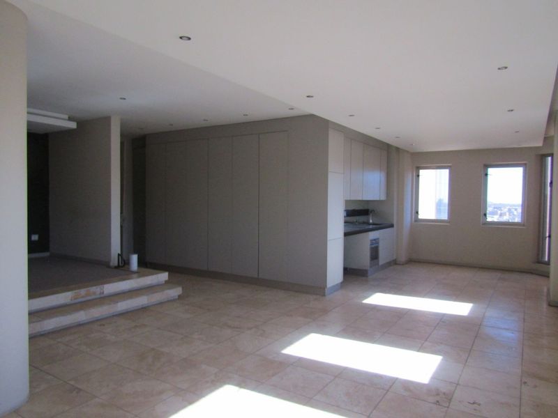 Spacious open-plan living area featuring stone tile flooring, recessed lighting, a raised platform, and a compact built-in kitchen unit with integrated oven.