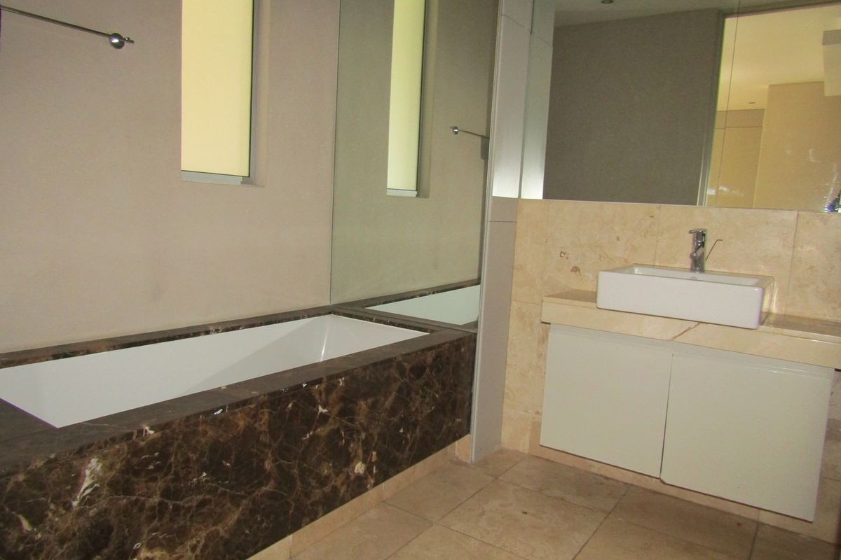Modern bathroom featuring a marble-clad built-in bathtub, a vessel sink with vanity cabinet, and large wall-mounted mirrors.